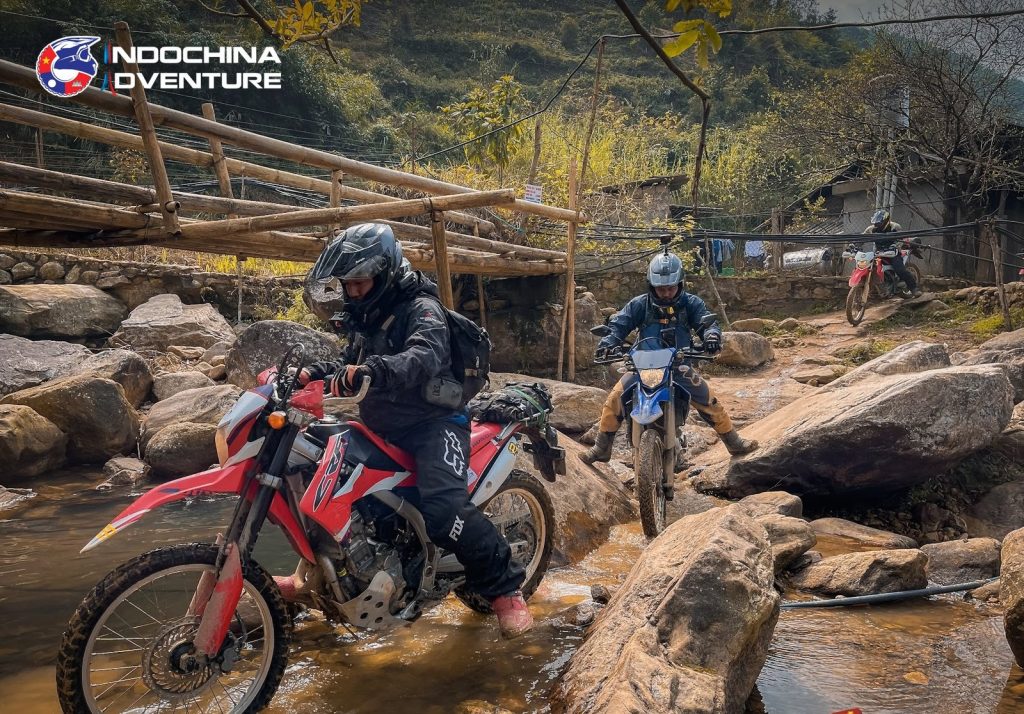 Guided motorbike tour group crossing a shallow river on a Vietnam offroad route
